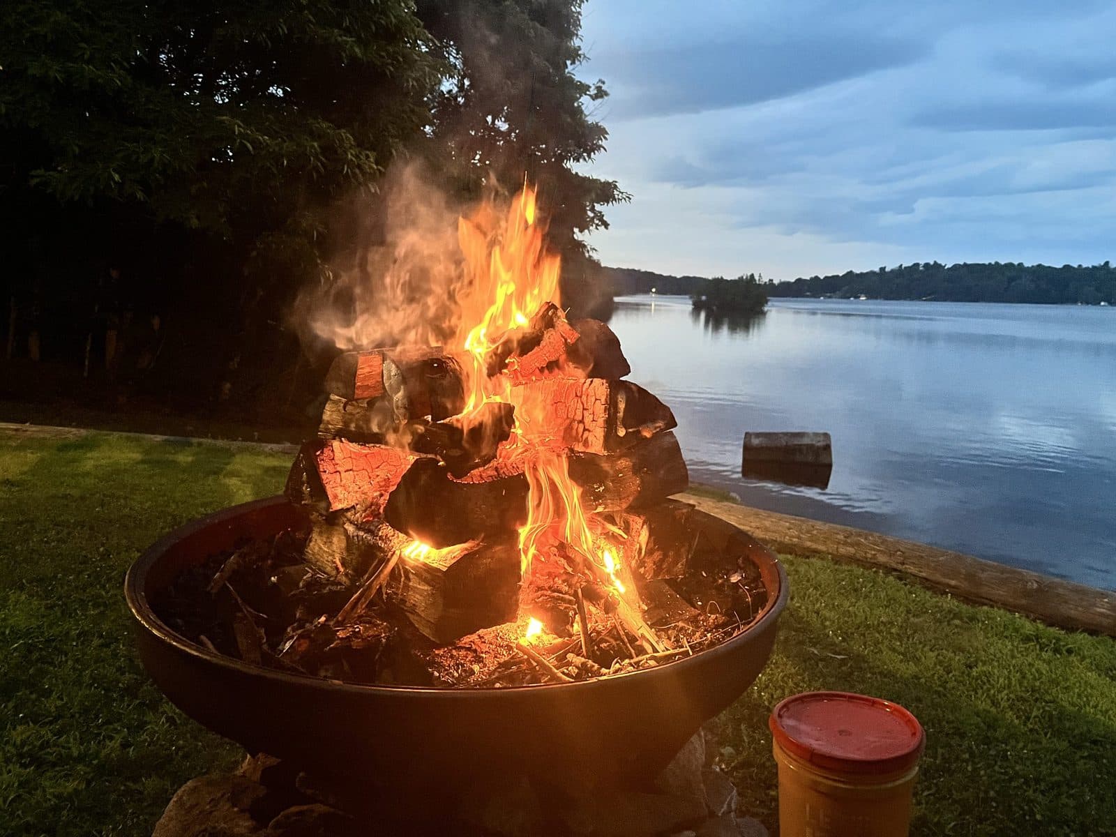 A campfire burning in a fire ring on the shore of the lake at dusk