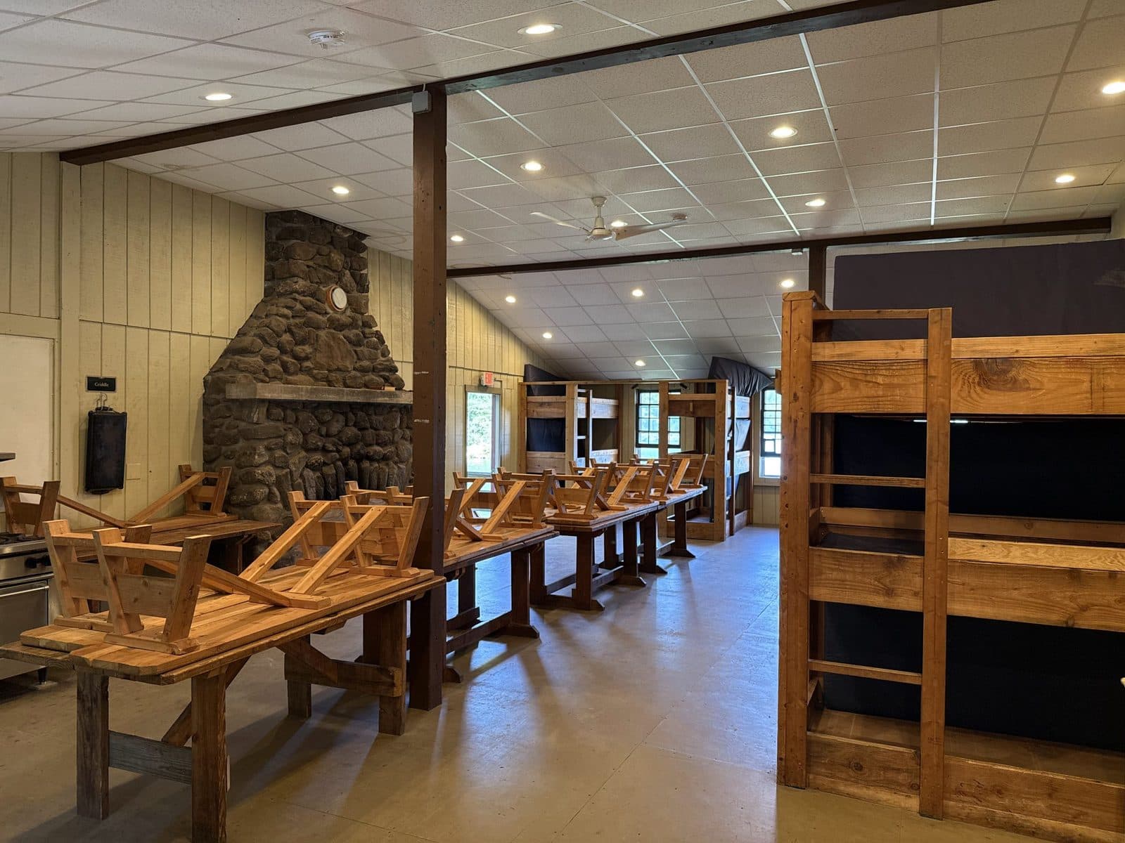 Inside Loomis Hall: wooden bunk beds and dining tables beside a tall stone fireplace